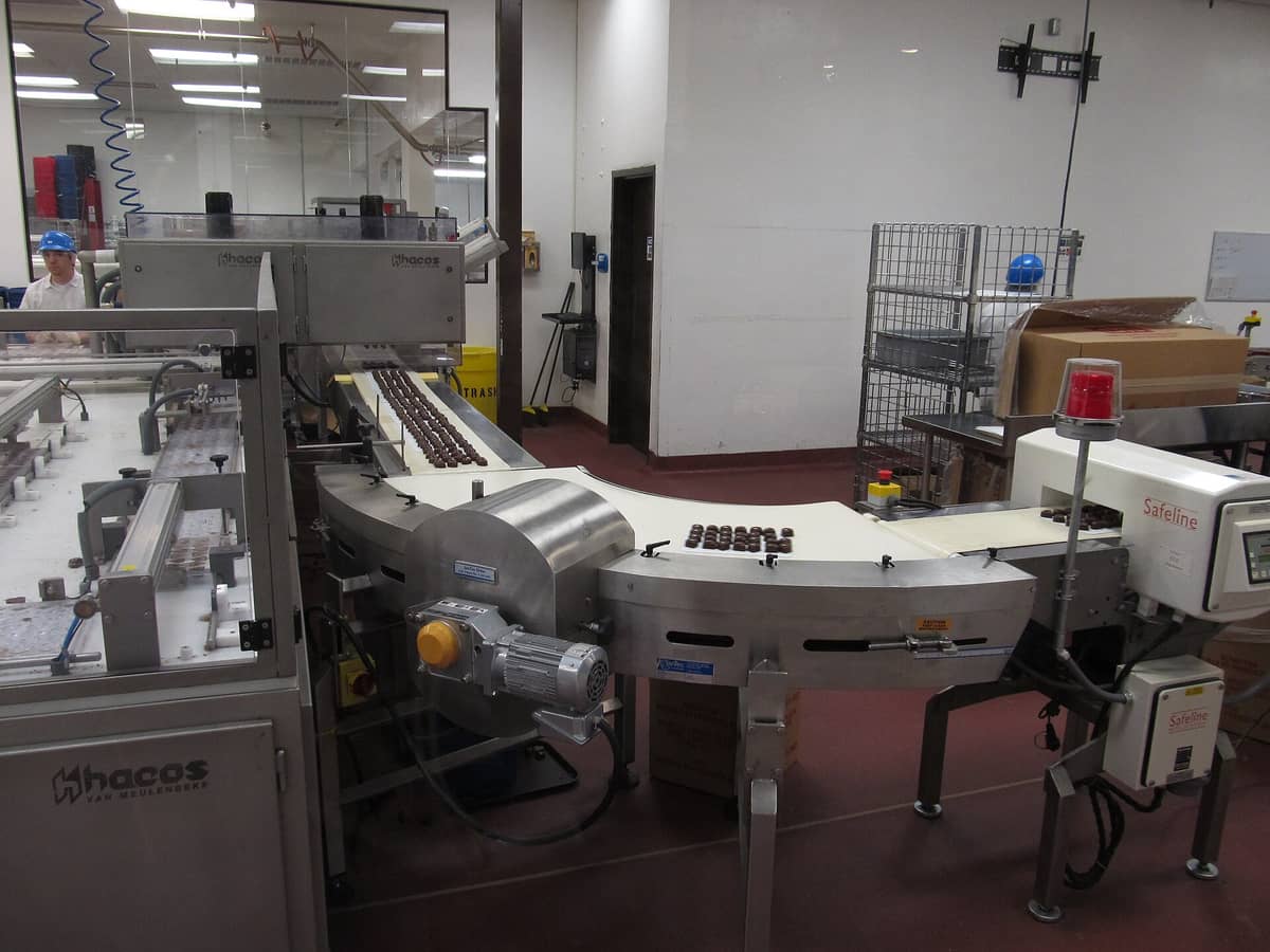 Lini produksi cokelat di dalam Ethel M Chocolates Factory, menampilkan cokelat di atas konveyor dan mesin-mesin di area pabrik.