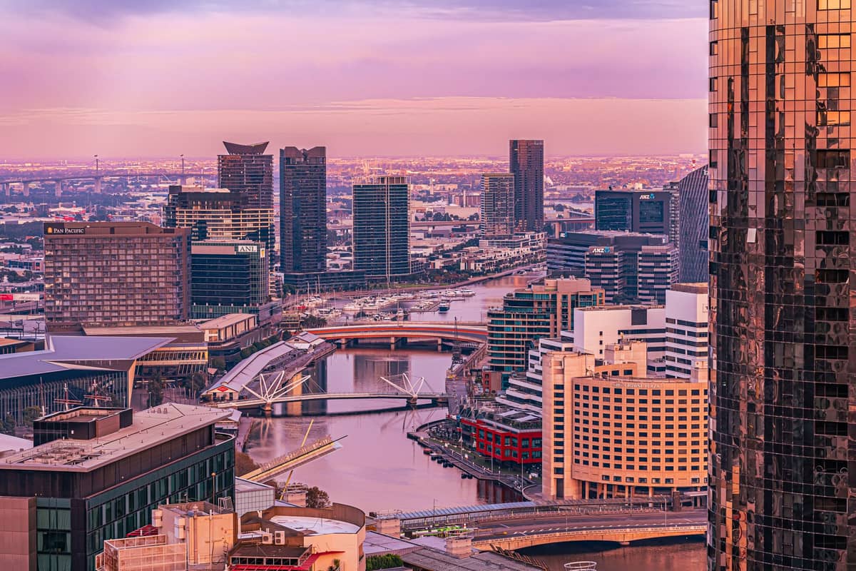 Vista panorámica desde el Melbourne Skydeck con el río Yarra, los puentes y los rascacielos modernos de la ciudad al atardecer, con un cielo violeta y rosado.