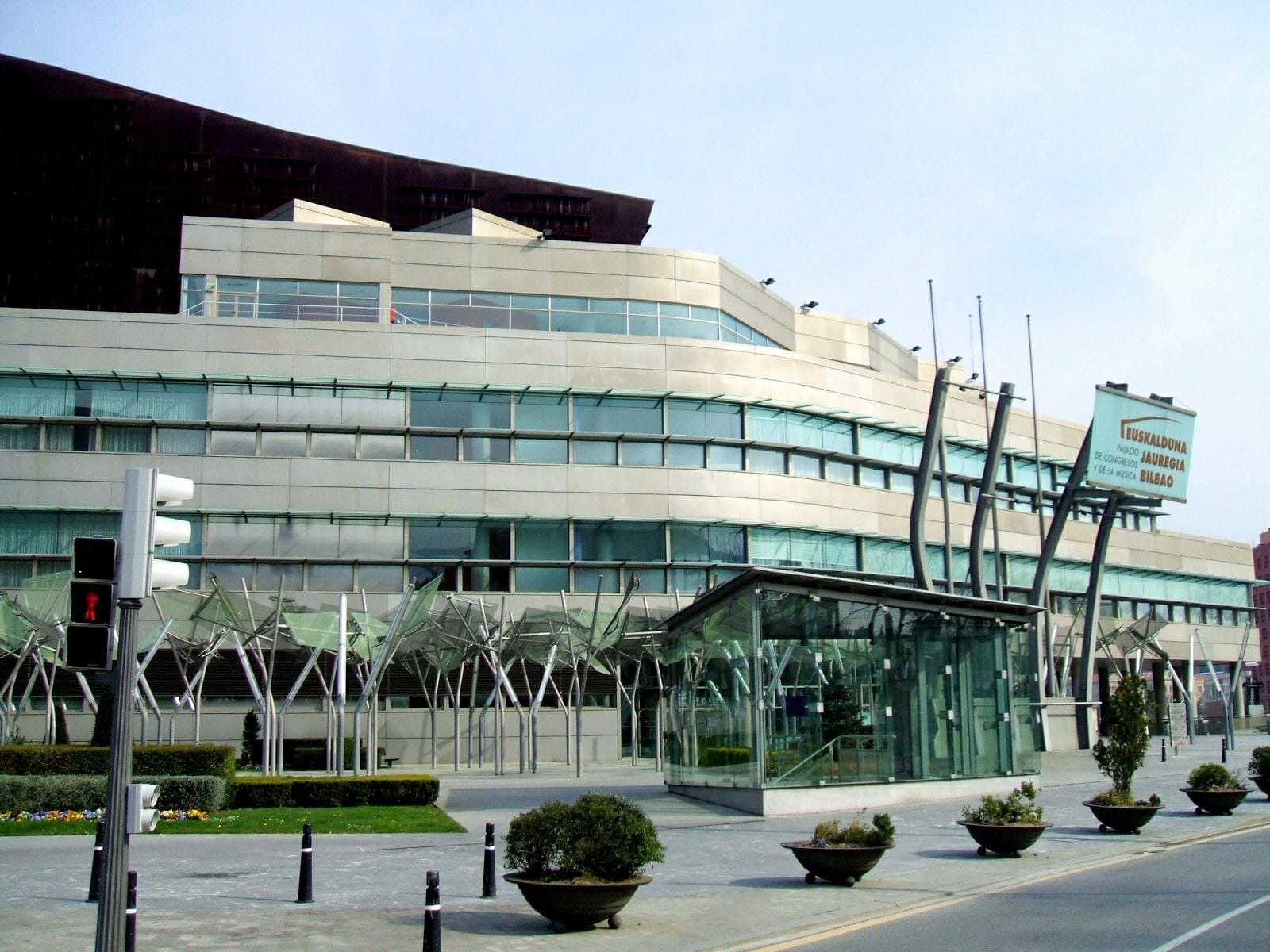 The Euskalduna Conference Centre and Concert Hall in Bilbao, featuring modern glass and metal architecture, street landscaping, and a clear blue sky.