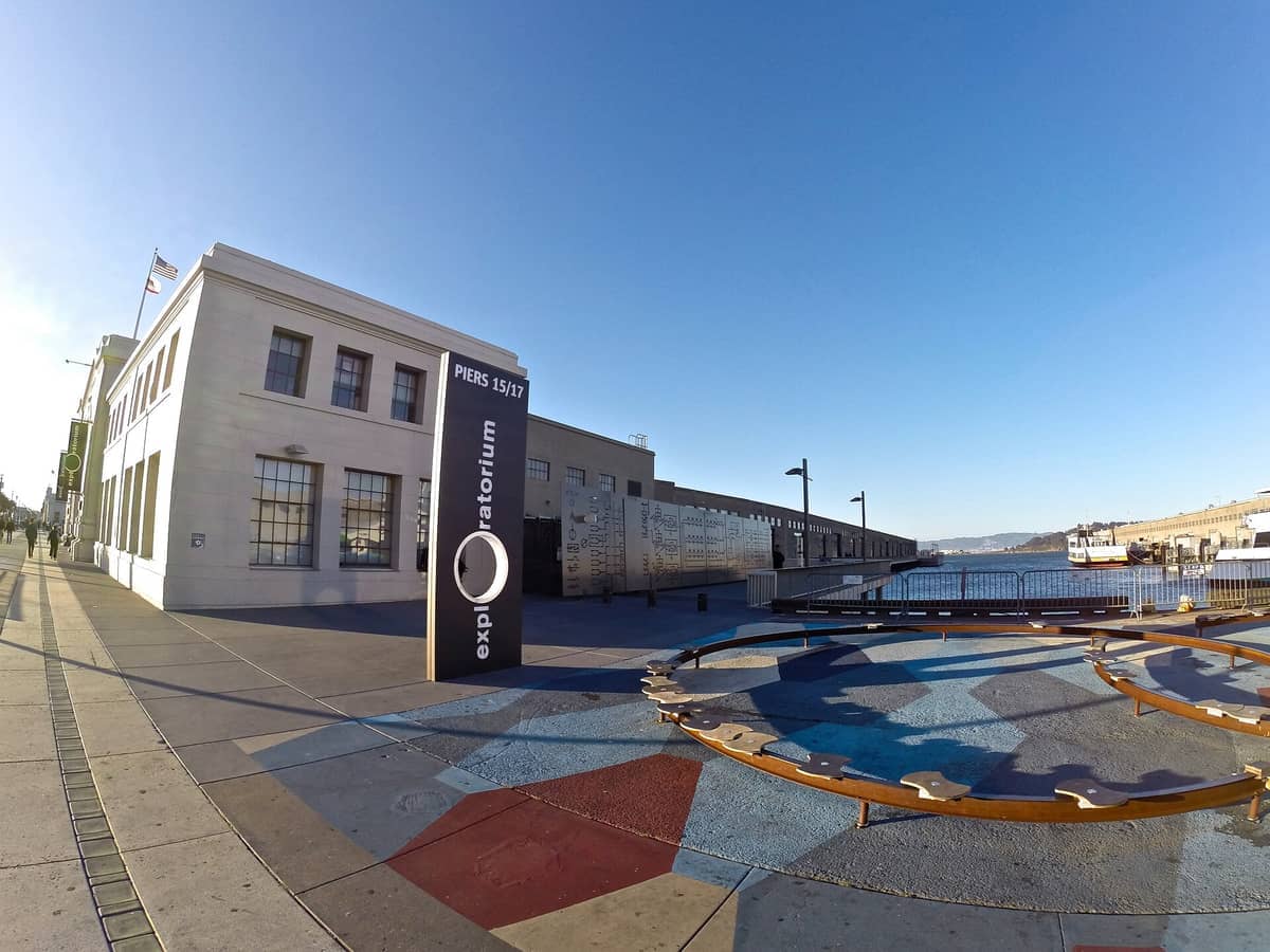 Das Äußere des Exploratoriums am Pier 15 in San Francisco, mit moderner Beschilderung, weißer Gebäudefassade und blauem Himmel über der Uferpromenade.