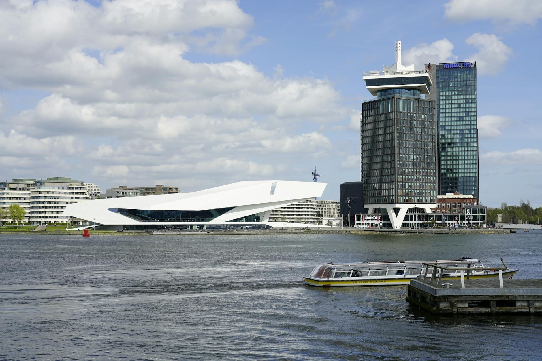 El singular edificio blanco y angular del Eye Filmmuseum y la torre A'DAM vistos desde el otro lado del río IJ bajo un cielo parcialmente nublado en Ámsterdam.