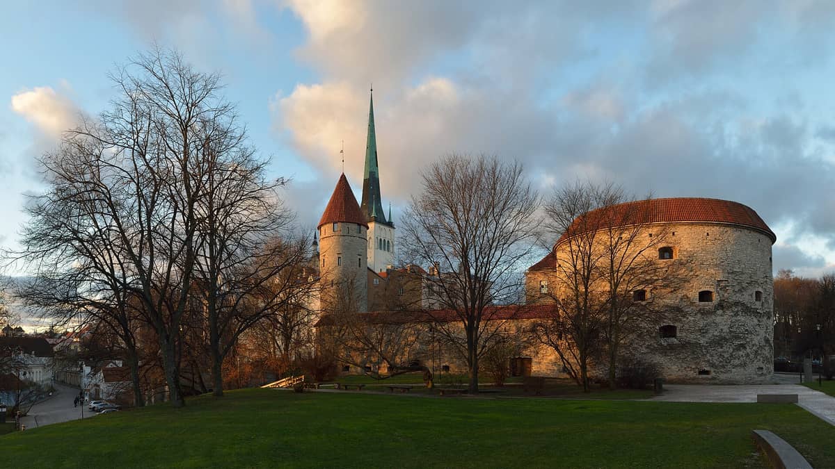 Panoramablick auf den Turm Dicke Margarete in Tallinn, Estland, bei Sonnenuntergang mit seinen runden Steinmauern und dem roten Ziegeldach, neben Stadtmauer und Kirchturm.