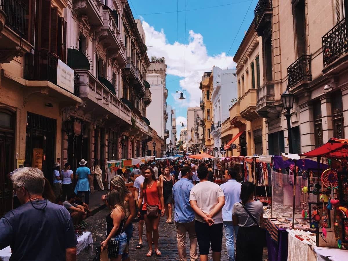 บรรยากาศตลาดกลางแจ้งคึกคักริม Calle Defensa ที่ Feria de San Telmo มีร้านแผงลอยสีสัน ผู้คนแน่นขนัด และอาคารประวัติศาสตร์สไตล์บัวโนสไอเรส