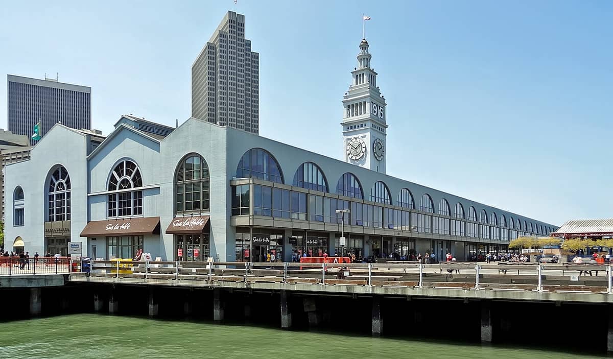 Il Ferry Building di San Francisco visto dall'acqua, con la sua iconica torre dell'orologio e la facciata sul lungomare, sullo sfondo dei grattacieli del centro.