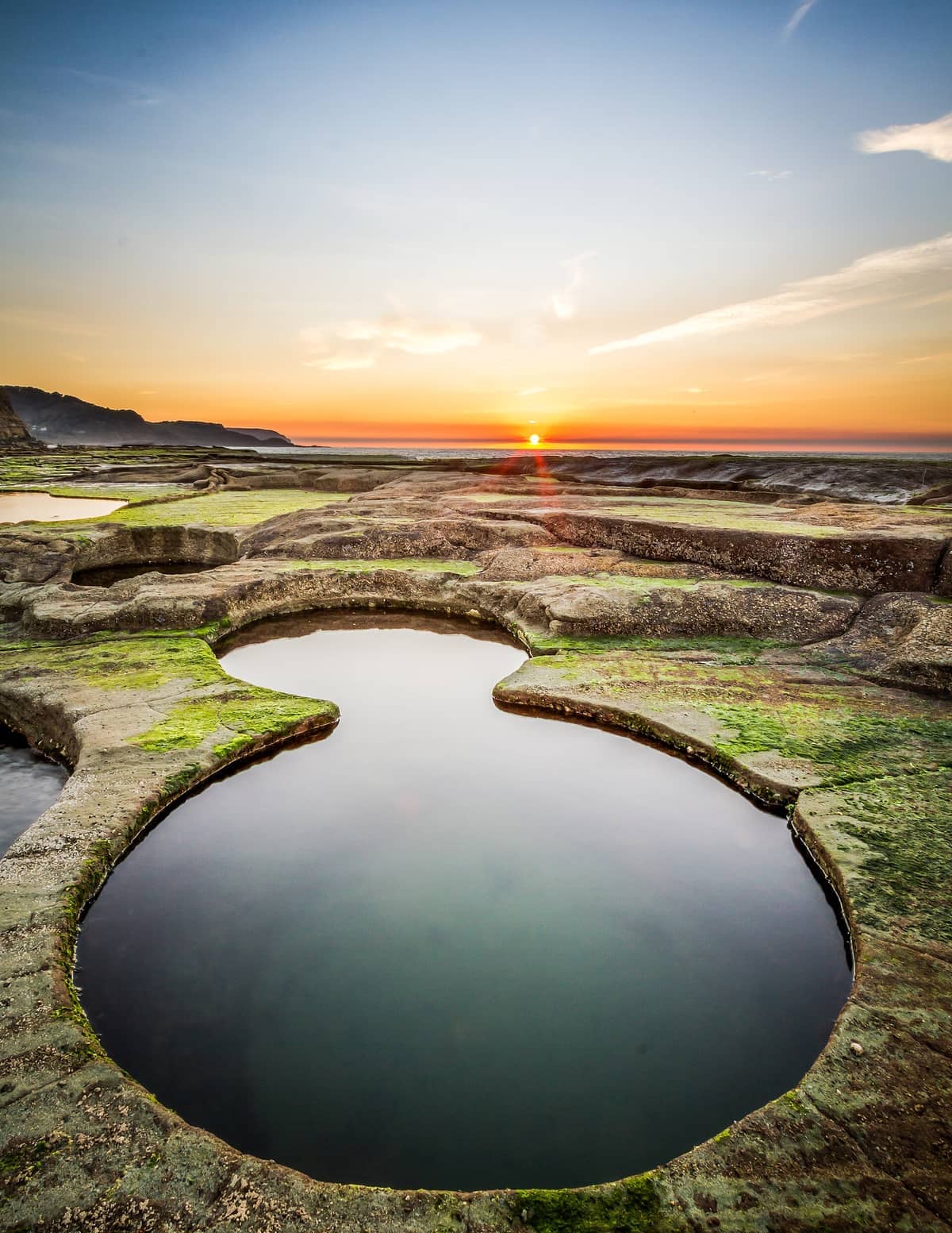 Figure Eight Pools in Royal National Park at sunrise, with naturally formed rock pools, mossy stone, and a clear, calm sky.