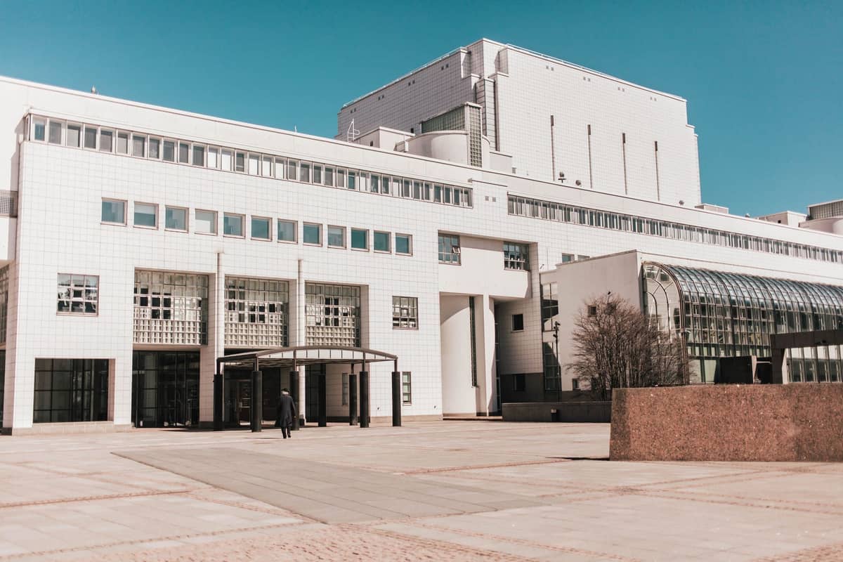 A moderna fachada branca do edifício da Ópera Nacional Finlandesa e Ballet em Helsinque sob um céu azul claro, com uma pessoa solitária entrando.
