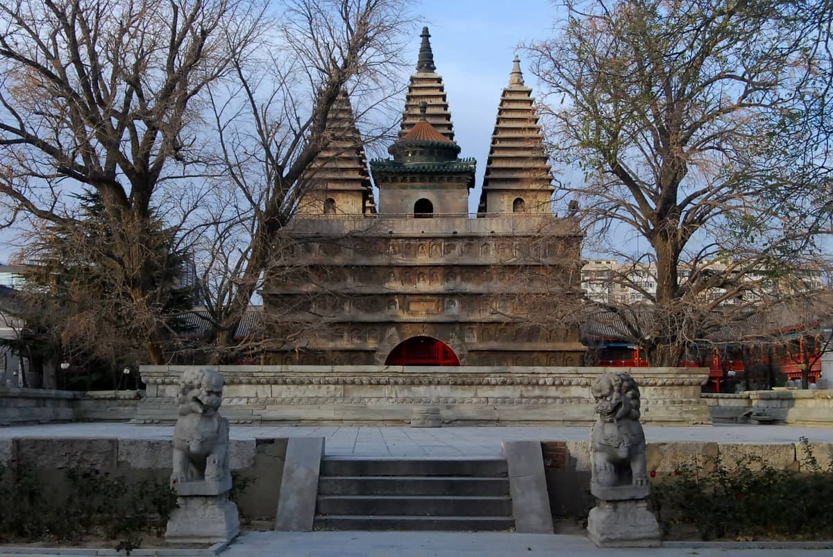Der Fünf-Pagoden-Tempel in Peking, umrahmt von blattlosen Bäumen und steinernen Löwenstatuen, mit klarem Himmel über seinen einzigartigen architektonischen Türmen.