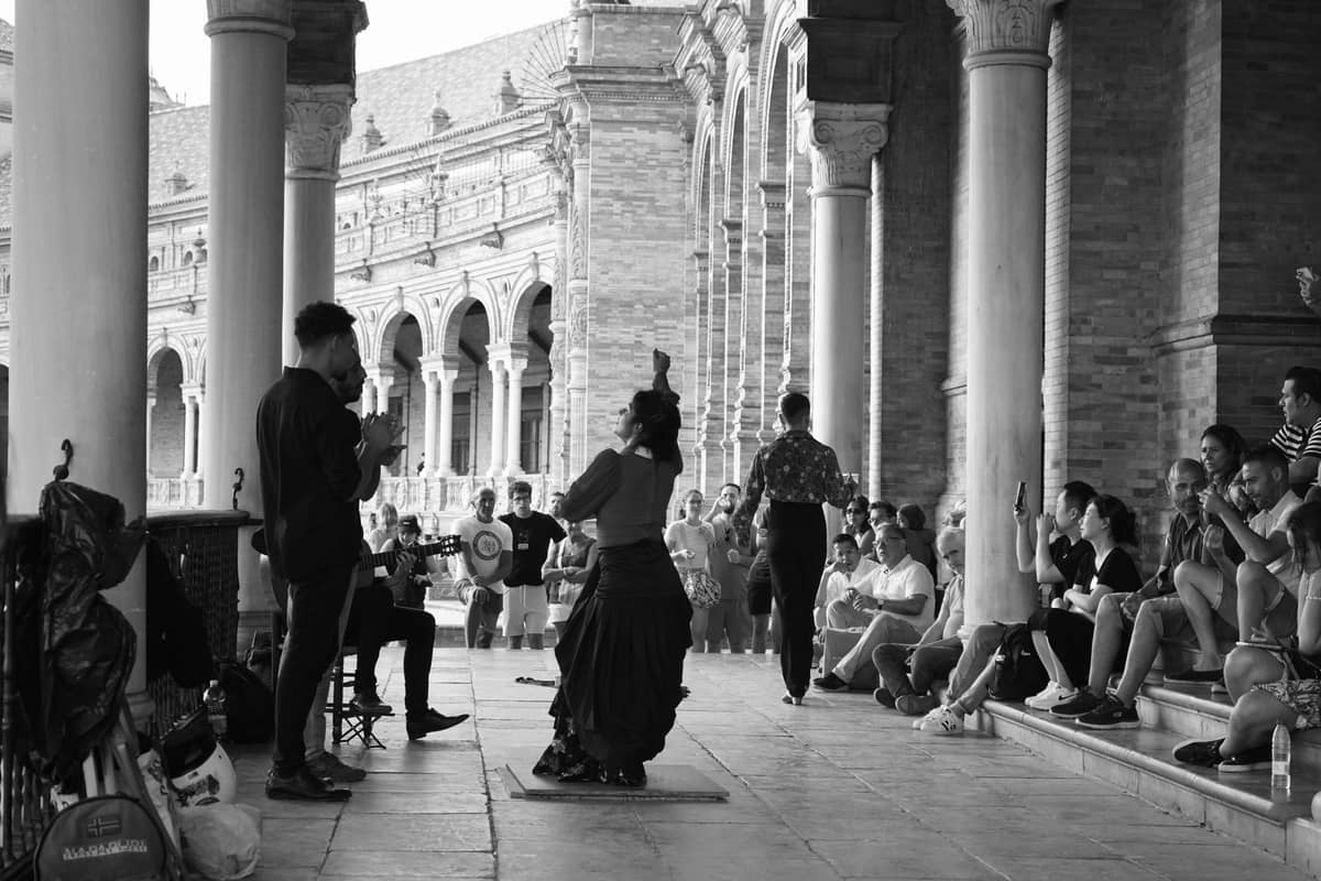 ภาพขาวดำของนักเต้นฟลาเมงโกแสดงต่อหน้าผู้ชมนั่งดู ใต้ซุ้มโค้ง Plaza de España เมืองเซบีญา