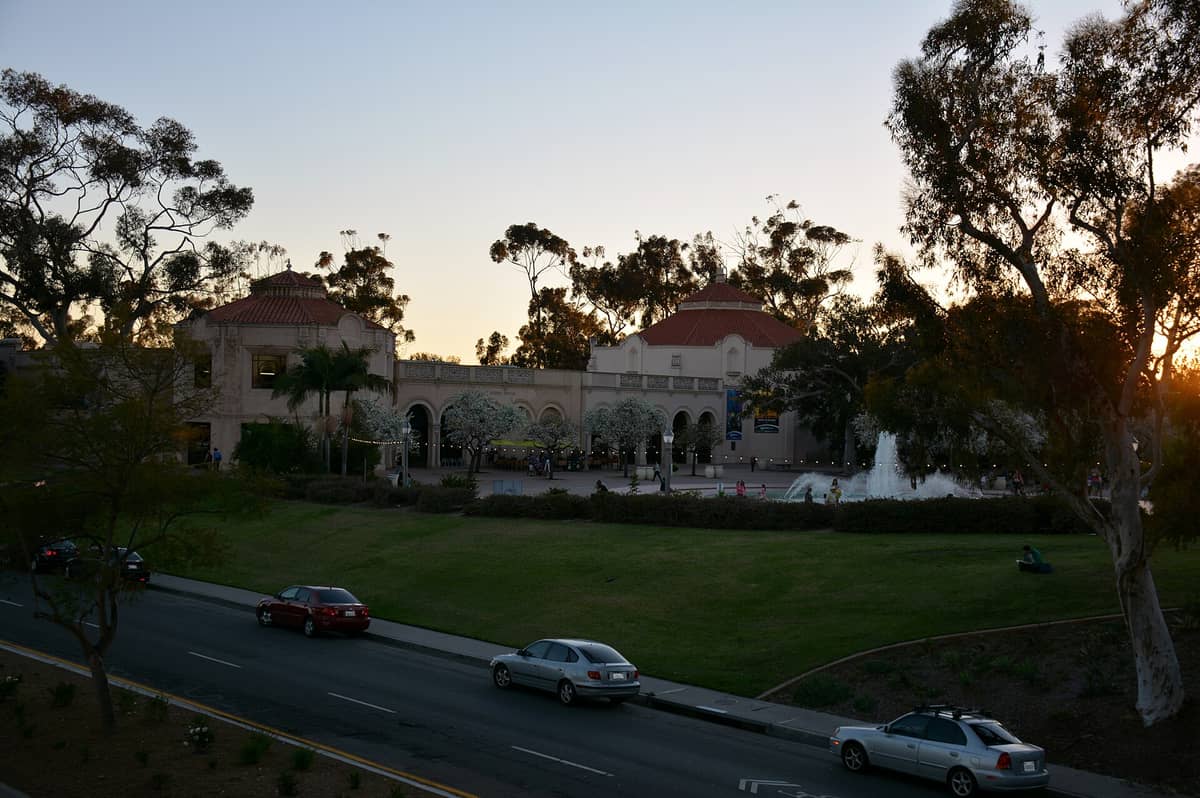 บรรยากาศด้านหน้า Fleet Science Center ใน Balboa Park ช่วงพระอาทิตย์ตก มีซุ้มทางเข้า ต้นไม้ น้ำพุ และผู้คนกำลังเดินเล่น