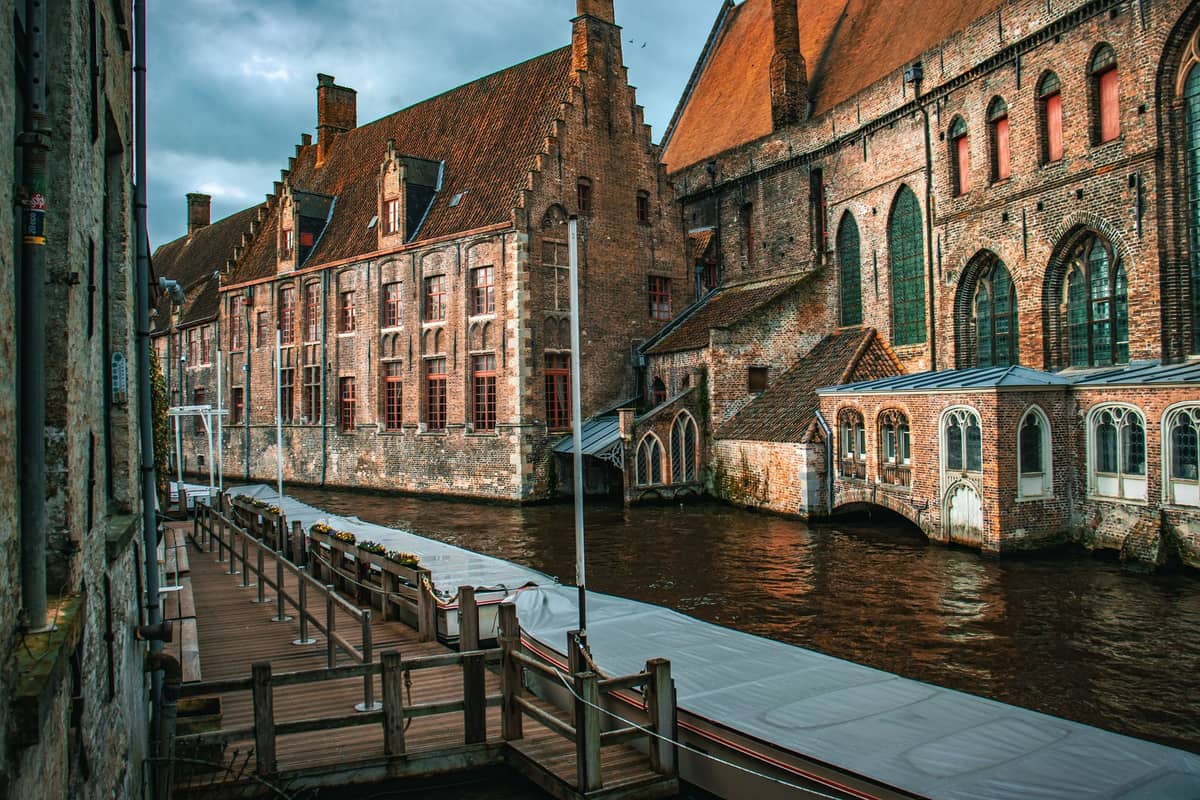 View of the historic Sint-Janshospitaal building with canal and empty dock in Bruges, under soft natural light, suggesting quieter visitor periods.