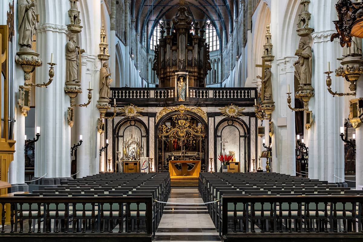 Nave and ornate altar of the Church of Our Lady in Bruges with vaulted ceilings, sculptures, and intricate organ visible.