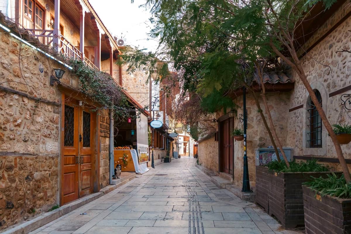 A quiet cobbled street lined with stone historic buildings and small shops in Antalya’s old town district Kaleiçi, under soft daylight.