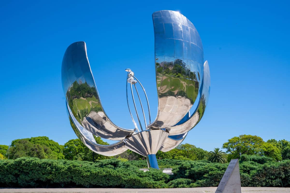 Floralis Genérica ดอกไม้เหล็กยักษ์กลางบัวโนสไอเรส กำลังบานกลางแจ้ง ใต้ท้องฟ้าสีฟ้า ต้นไม้เขียวสดอยู่เบื้องหลัง
