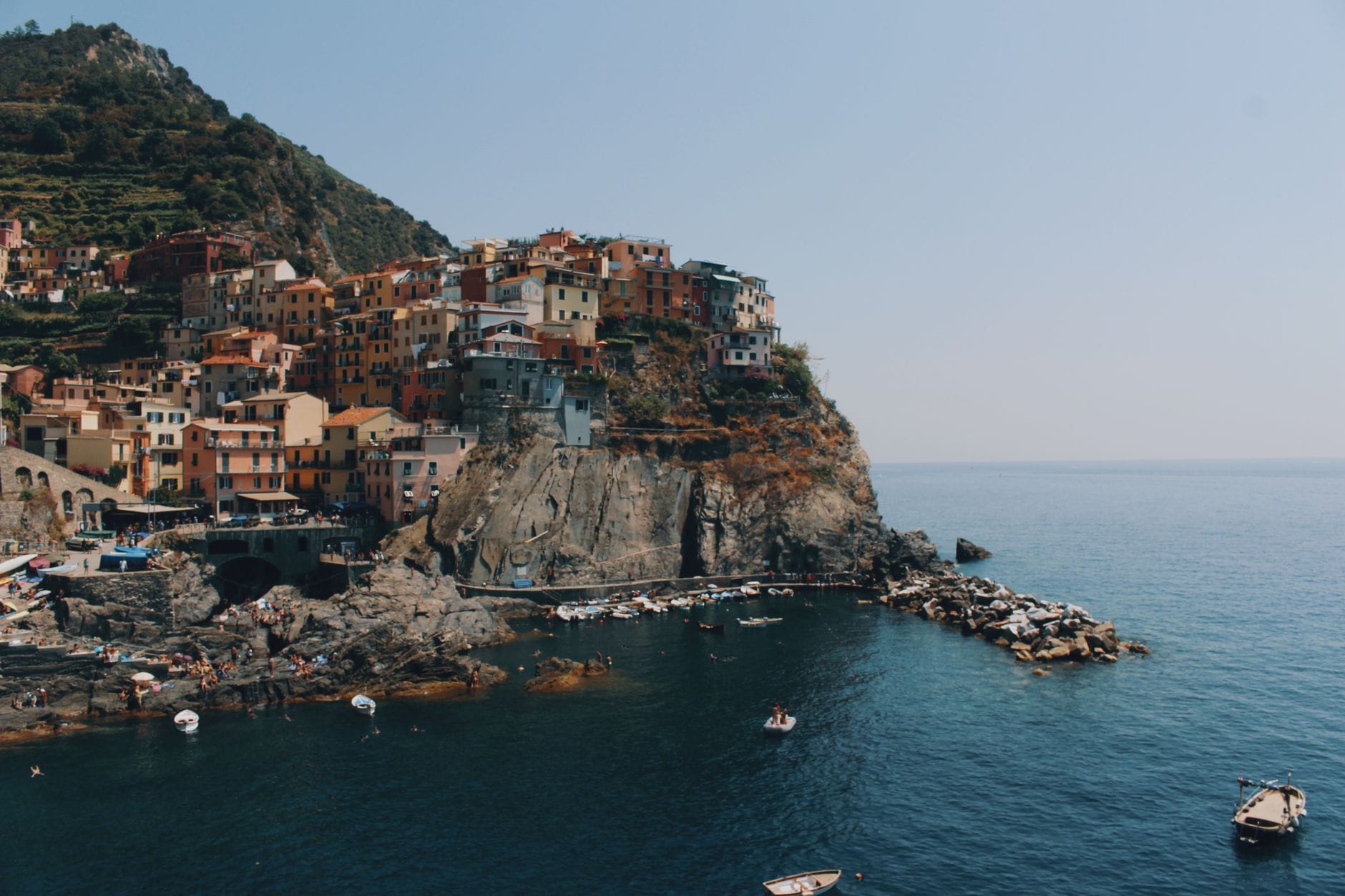 หมู่บ้านริมหน้าผา Manarola ในชิงเกวแตร์เร่ สีสันสดใสริมทะเล มีเรือลอยน้ำและชายฝั่งหินด้านล่าง