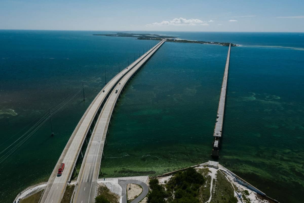 Aerial view of the Overseas Highway stretching across turquoise water towards distant islands, with modern and old parallel bridges visible.