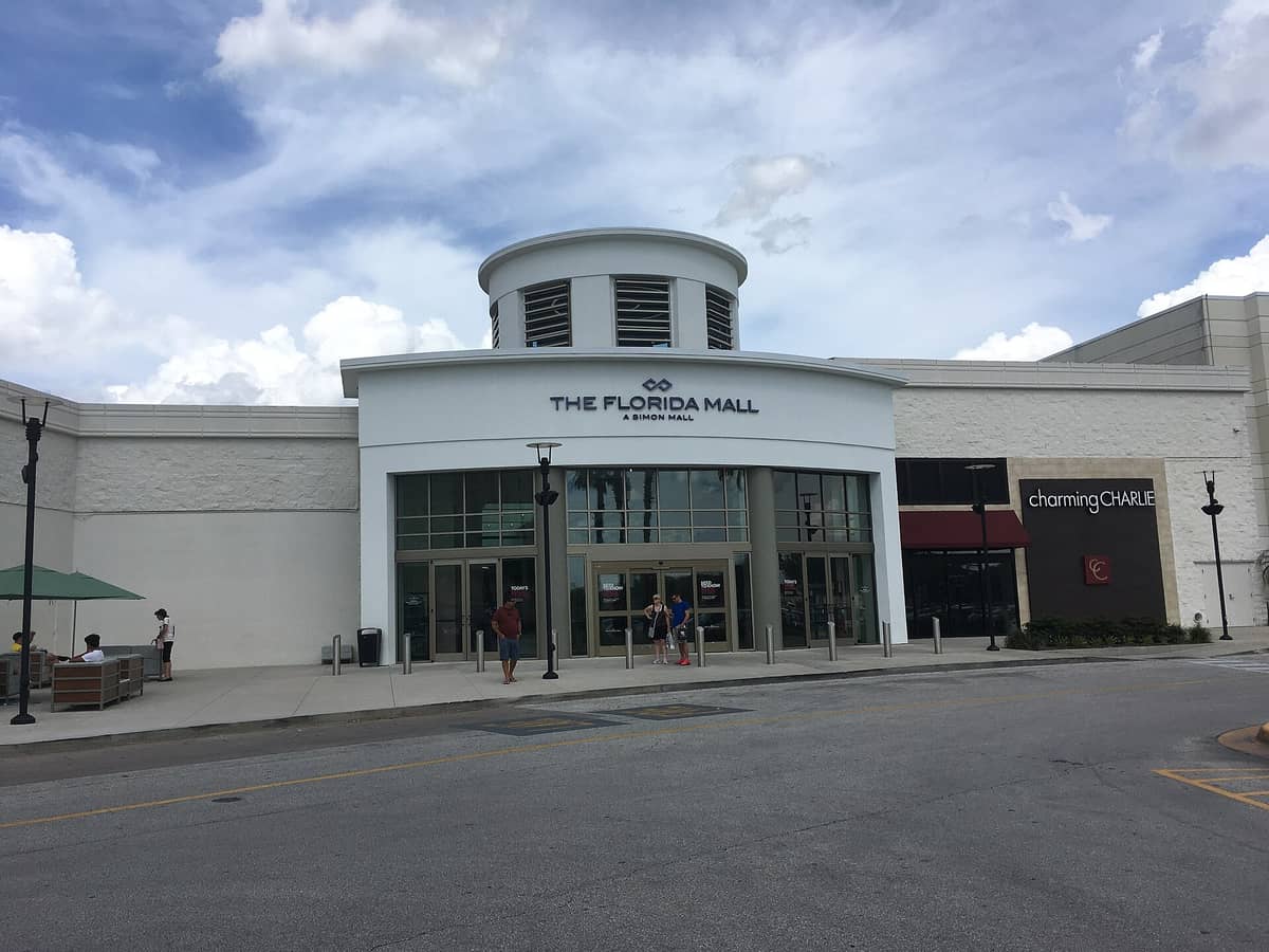 Exterior entrance of The Florida Mall in Orlando, showing the mall's name above glass doors and a few people near the entrance.