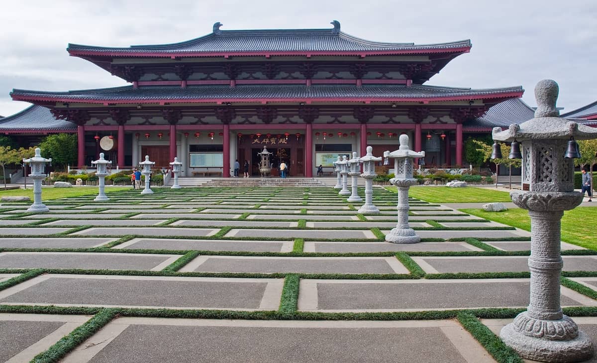 Buddhistischer Tempel Fo Guang Shan in Auckland mit Tang-Stil-Architektur, Steinlaternen, gepflegten Wegen und einem schattigen Innenhof unter bewölktem Himmel.