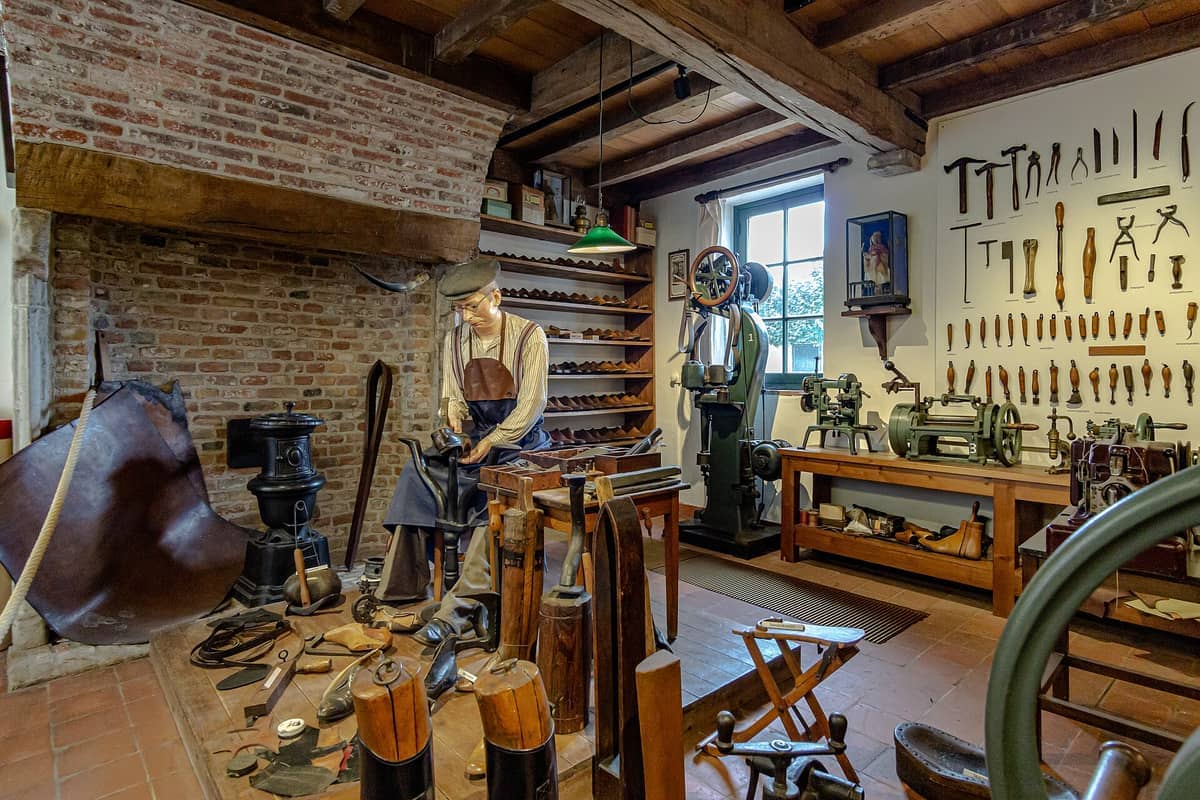 Historic cobbler's workshop at the Folklore Museum Bruges, featuring antique tools, leather goods, and a lifelike mannequin in period dress.