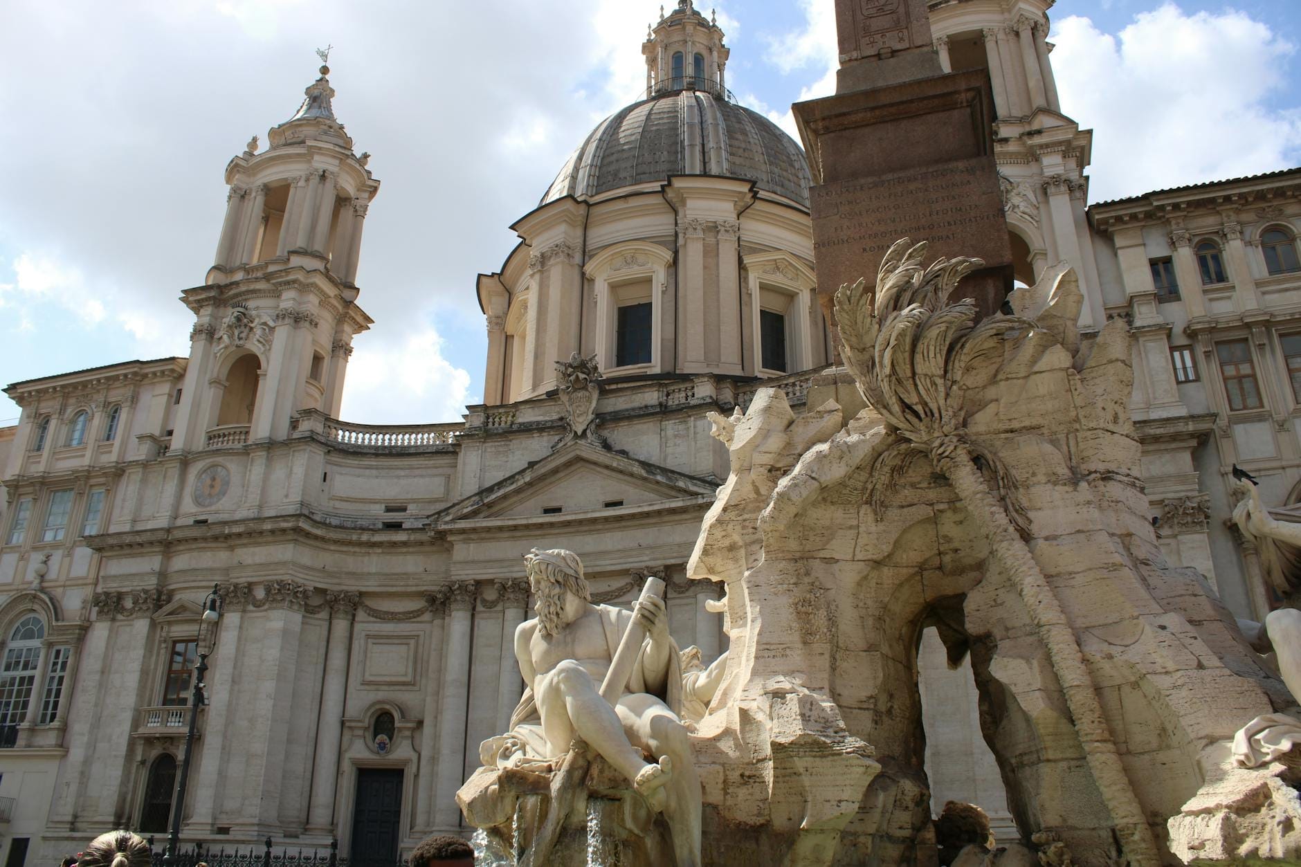 Wide view of the Fontana dei Quattro Fiumi with its dramatic statues, flowing water, the Egyptian obelisk, and Sant'Agnese in Agone church in Piazza Navona.