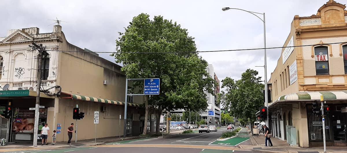 ถนนในย่าน Footscray ที่คึกคักเรียงรายด้วยอาคารประวัติศาสตร์ ต้นไม้ร่มรื่น คนเดินถนน รถยนต์จอดข้างทาง และร้านค้าภายใต้ท้องฟ้าครึ้ม