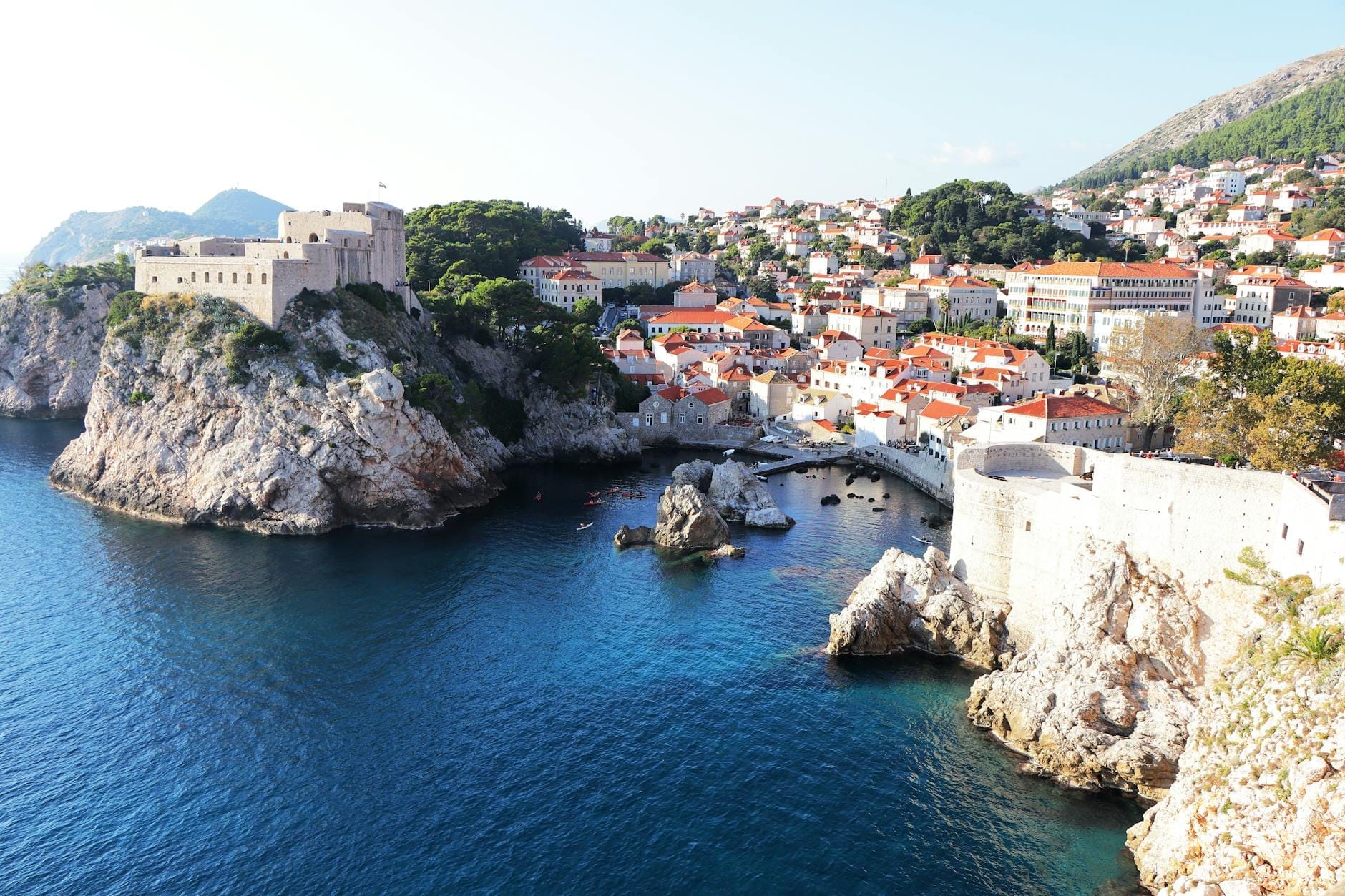 Vista panorámica del Fuerte Lovrijenac encaramado sobre un acantilado rocoso junto al mar, con el casco antiguo de Dubrovnik y el agua azul cristalina de fondo en un día soleado.
