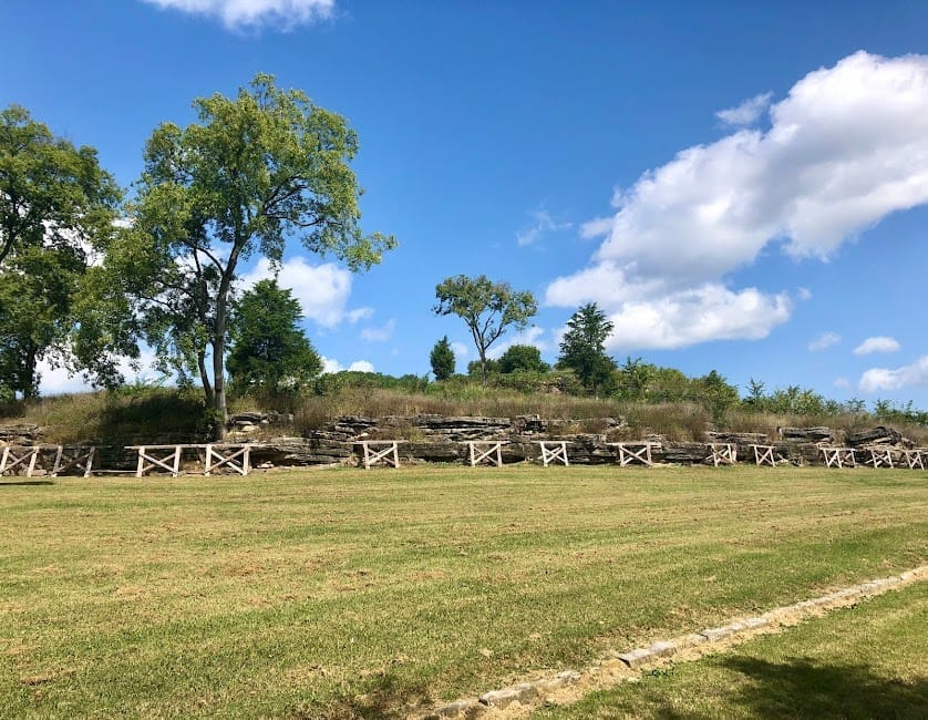 Vista amplia de los muros de piedra históricos y el campo de hierba del Fort Negley Park bajo un cielo azul brillante con nubes dispersas y árboles verdes.