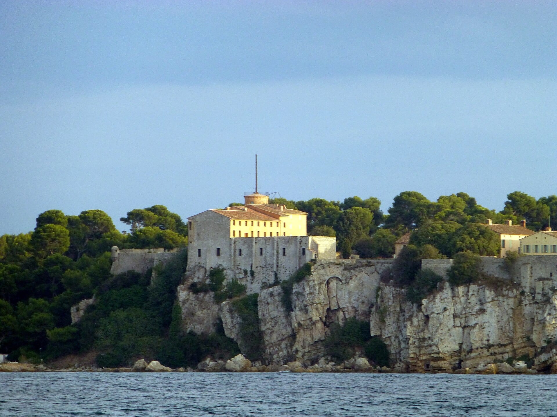 Fort Royal arroccato in cima a scogliere frastagliate sull'Île Sainte-Marguerite, circondato da fitti pini e affacciato sulle acque blu del Mediterraneo.