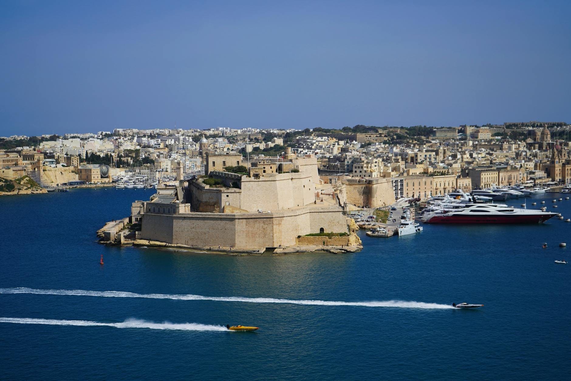 Vista panoramica di Fort Sant'Angelo che si protende nel Grand Harbour, circondato dall'acqua blu profonda, imbarcazioni e lo skyline di Birgu, Malta.