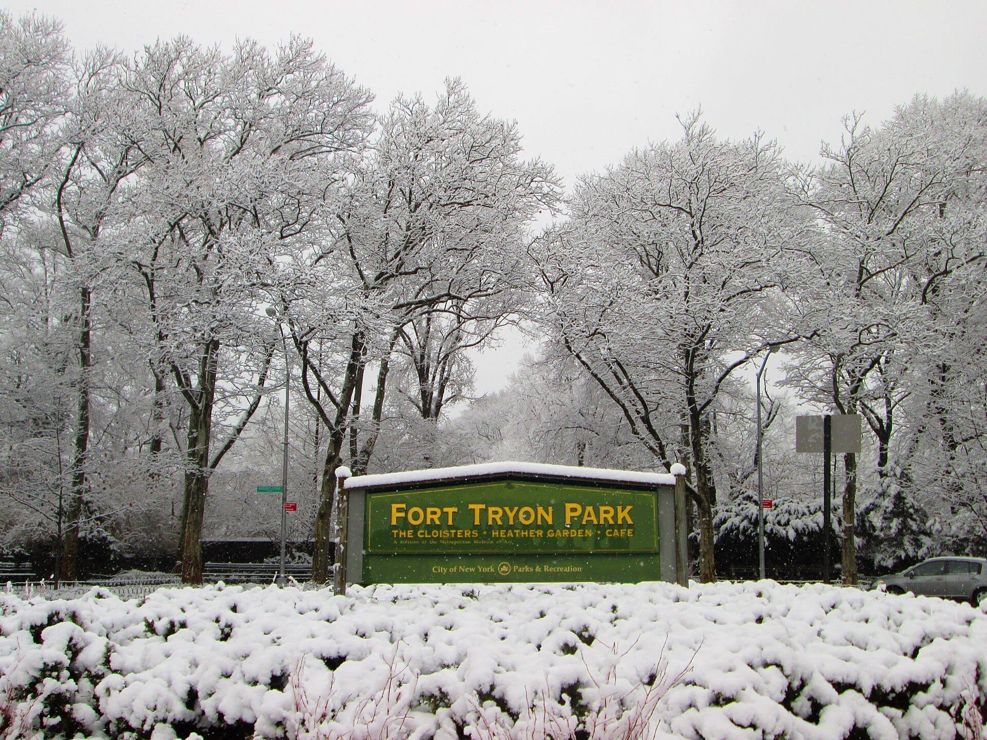Cartello d'ingresso del Fort Tryon Park circondato da alberi e cespugli innevati in una nuvolosa giornata invernale a Manhattan.