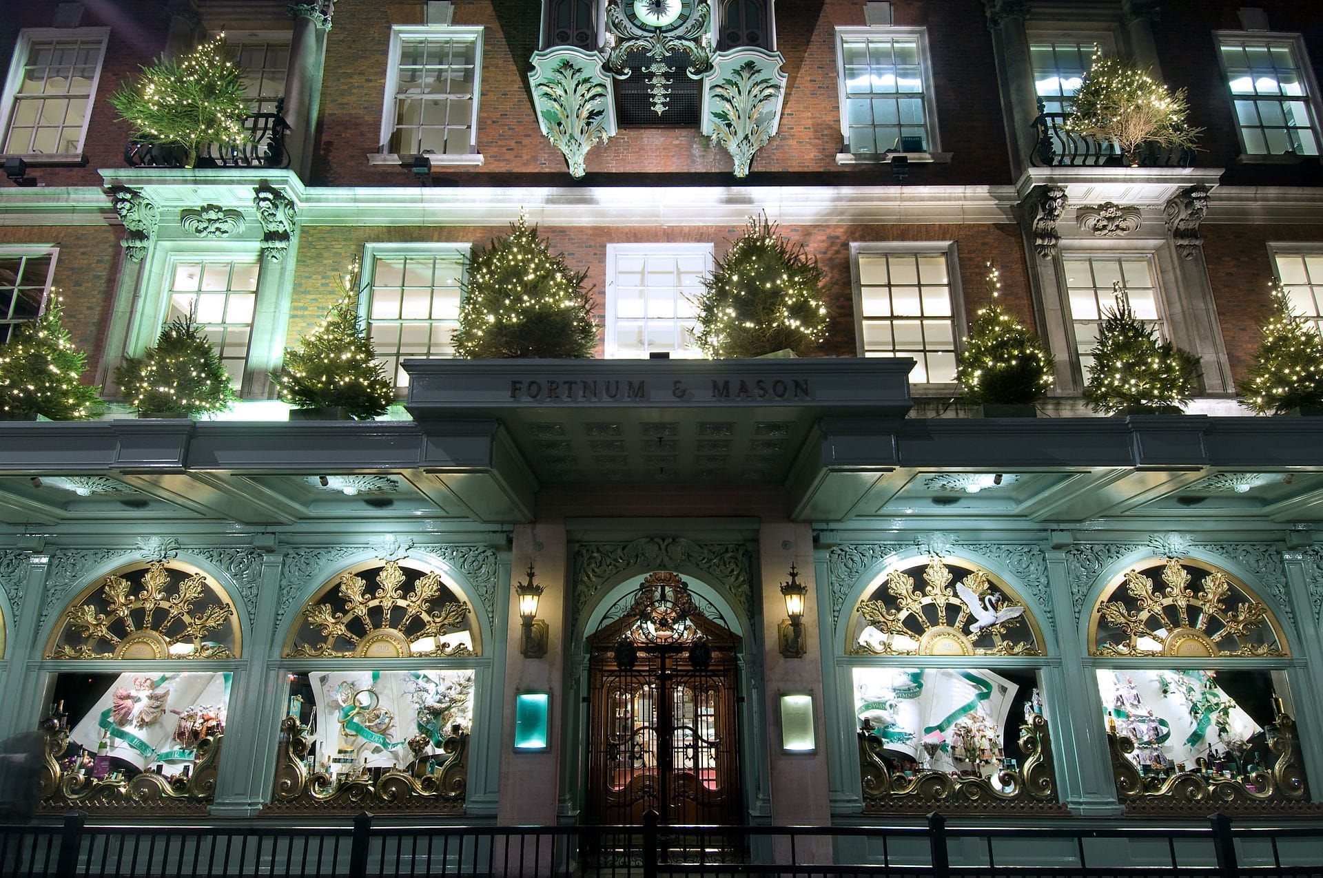 La facciata illuminata di Fortnum & Mason a Londra, adornata con alberi di Natale scintillanti ed eleganti vetrine di notte.