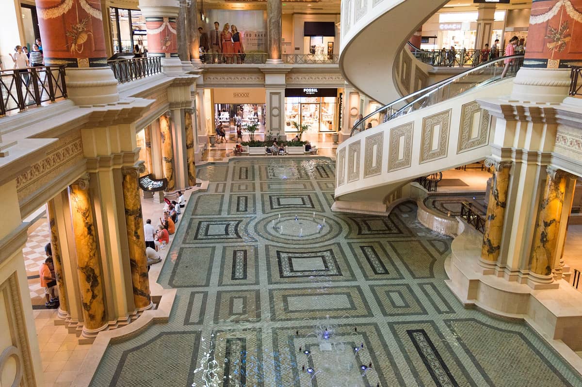 Widok na centralną fontannę i spiralne schody ruchome wewnątrz Forum Shops at Caesars Palace – rzymskie kolumny, elegancki wystrój i witryny luksusowych sklepów.