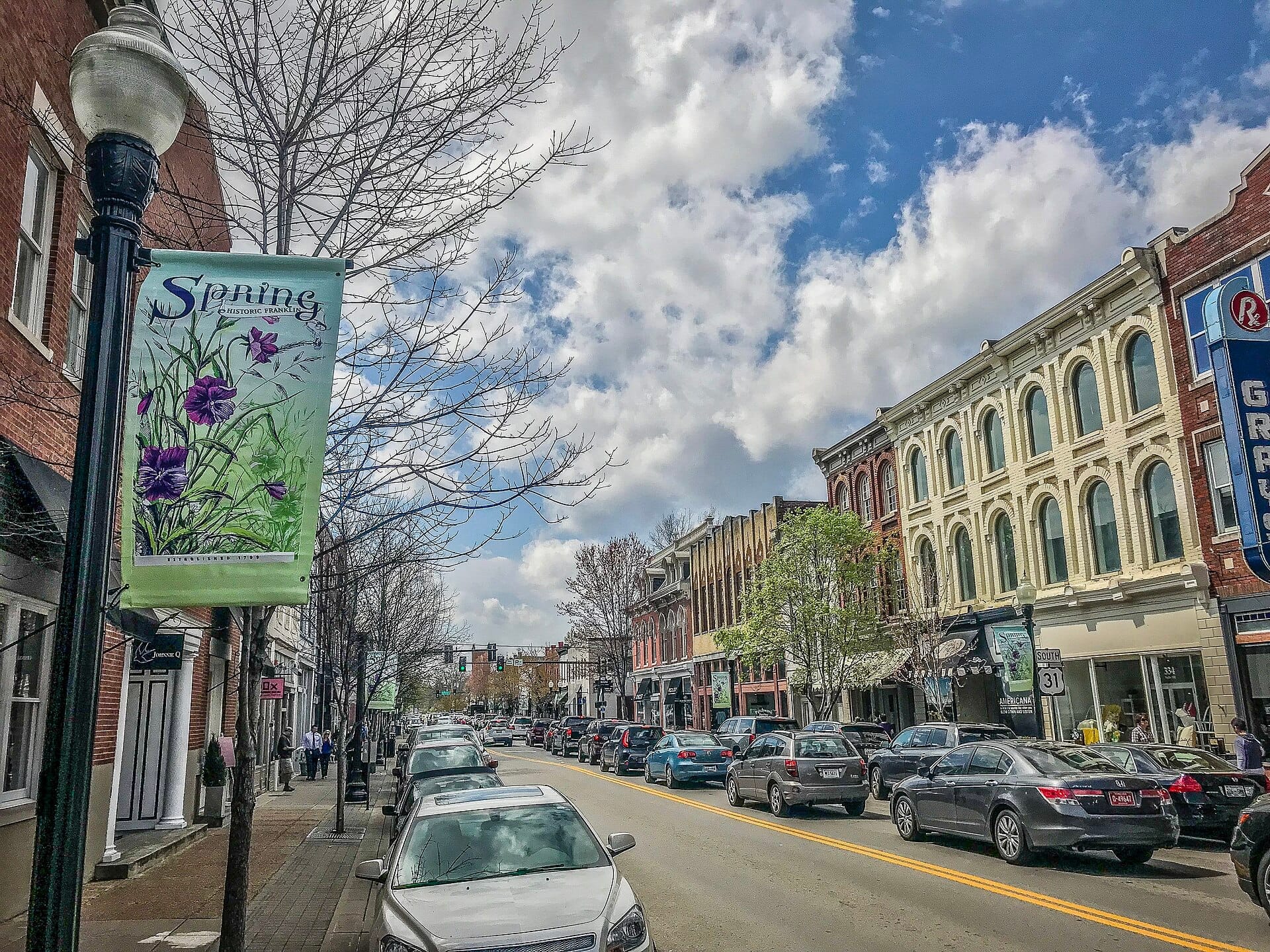Calle Main histórica en el centro de Franklin con hileras de edificios de ladrillo del siglo XIX, coches aparcados y una pancarta floral de primavera en un día soleado.