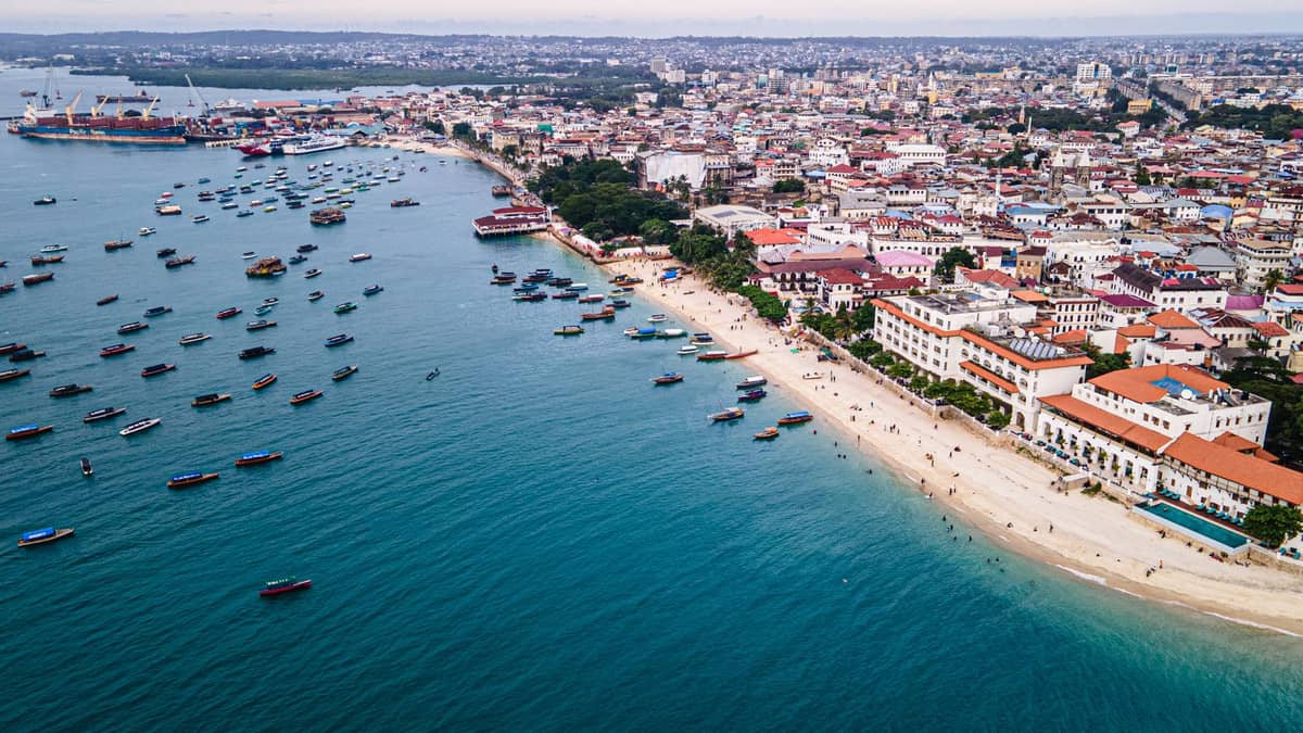 Aerial view of Stone Town coastline with beach, boats, historic buildings, and the city spreading inland in Zanzibar.