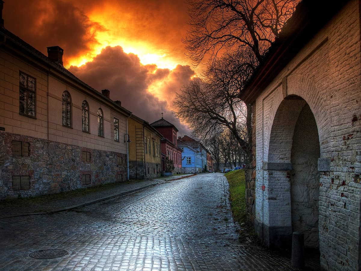 ถนนหินกรวดและอาคารประวัติศาสตร์ภายใน Fredrikstad Old Town พร้อมเมฆยามเย็นที่ดูตระการตาและแสงอาทิตย์อ่อนโยนส่องสว่างกำแพงหินและอิฐ