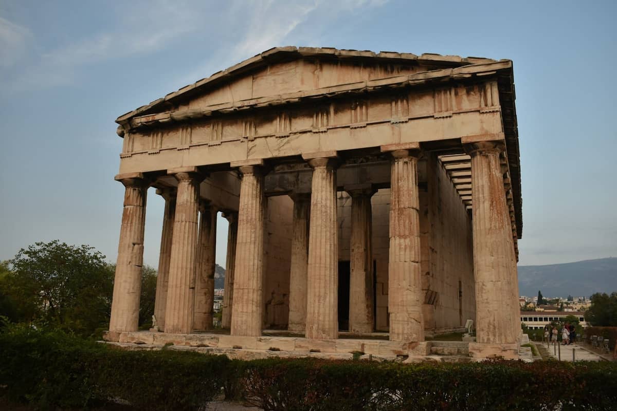 Antiker griechischer Tempel mit gut erhaltenen dorischen Säulen, umgeben von Grün unter blauem Himmel in Athen.