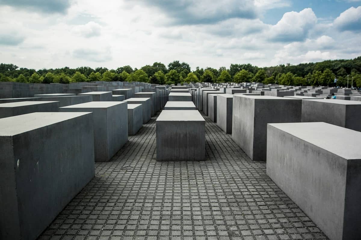 Vista amplia del Memorial a los Judíos Asesinados de Europa en Berlín, con estelas de hormigón y árboles al fondo bajo un cielo nublado.