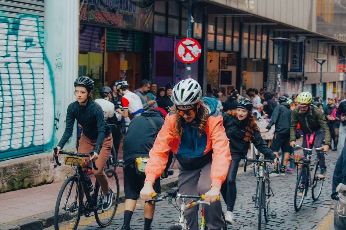 A large group of cyclists riding through a city street lined with graffiti and shops, evoking a car-free urban cycling event.