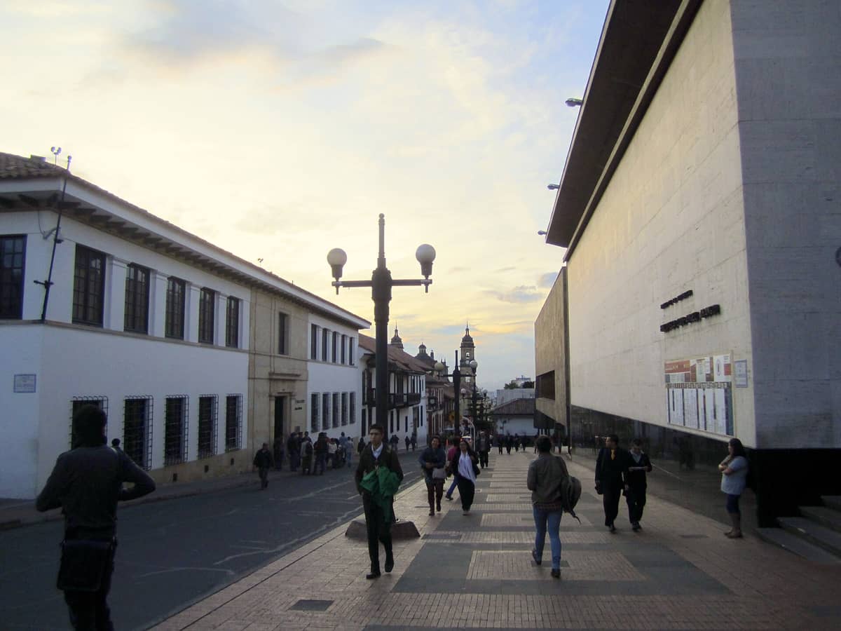 People walking near the entrance of the Museo del Oro on Calle 16 in Bogotá's La Candelaria district at sunset.