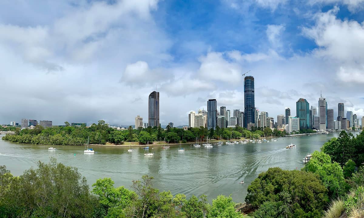 Vista amplia del horizonte de Brisbane con el río Brisbane en primer plano, varios barcos en el agua y abundante vegetación a orillas del río.