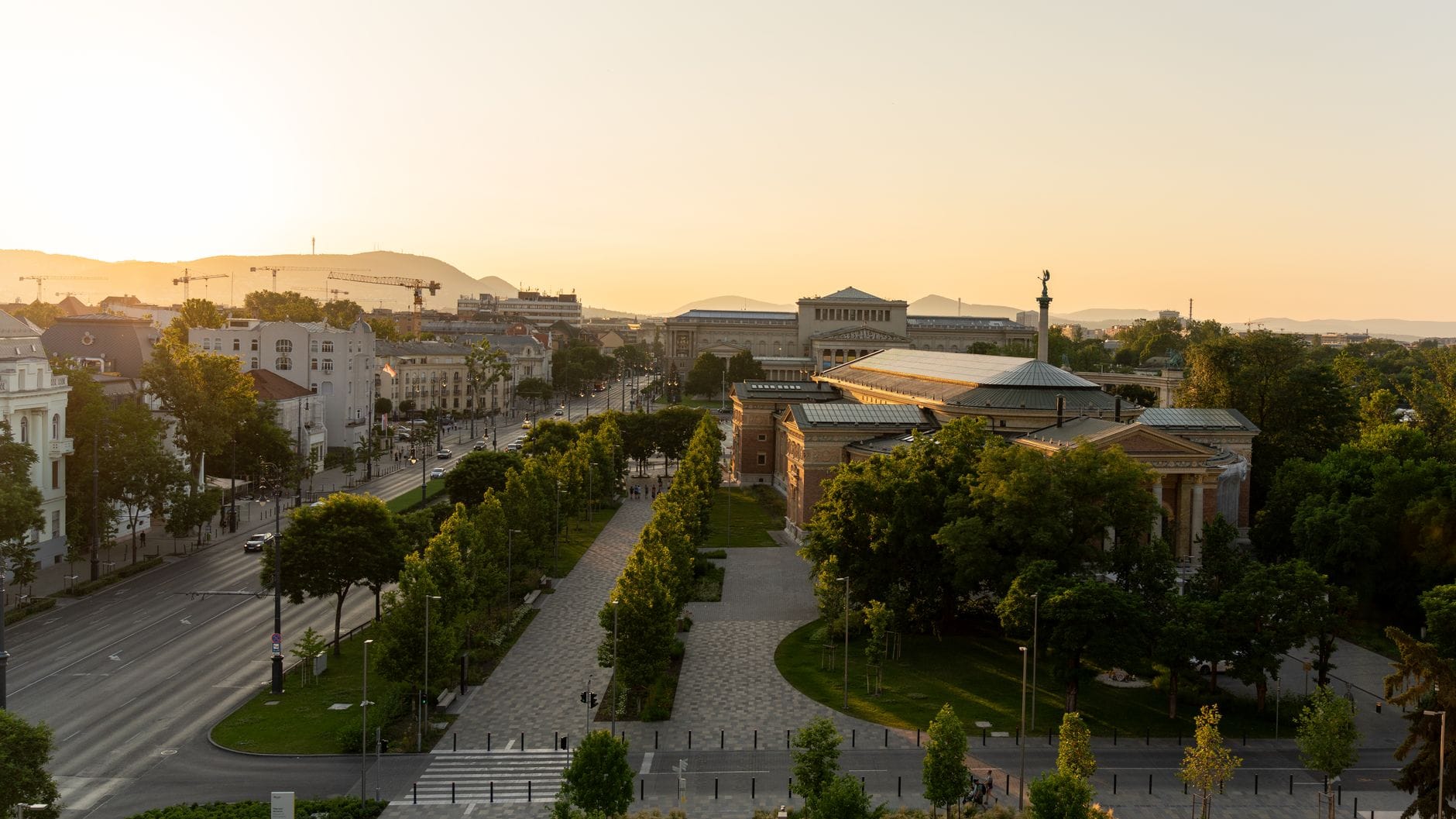 Luftaufnahme der prächtigen Andrássy Avenue in Budapest, die zum Heldenplatz führt, gesäumt von neorenaissance Gebäuden und üppigen grünen Bäumen bei Sonnenuntergang.