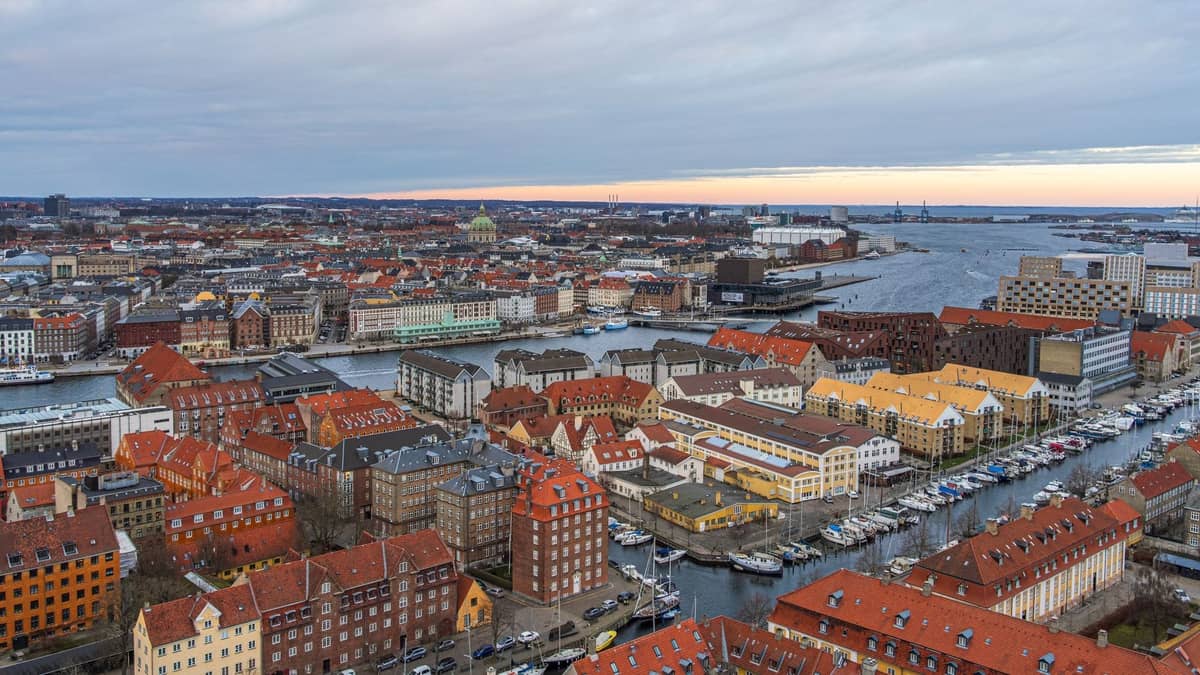 Vista aérea de Copenhague con coloridos edificios históricos, canales sinuosos y barrios urbanos bajo un cielo nublado al atardecer.