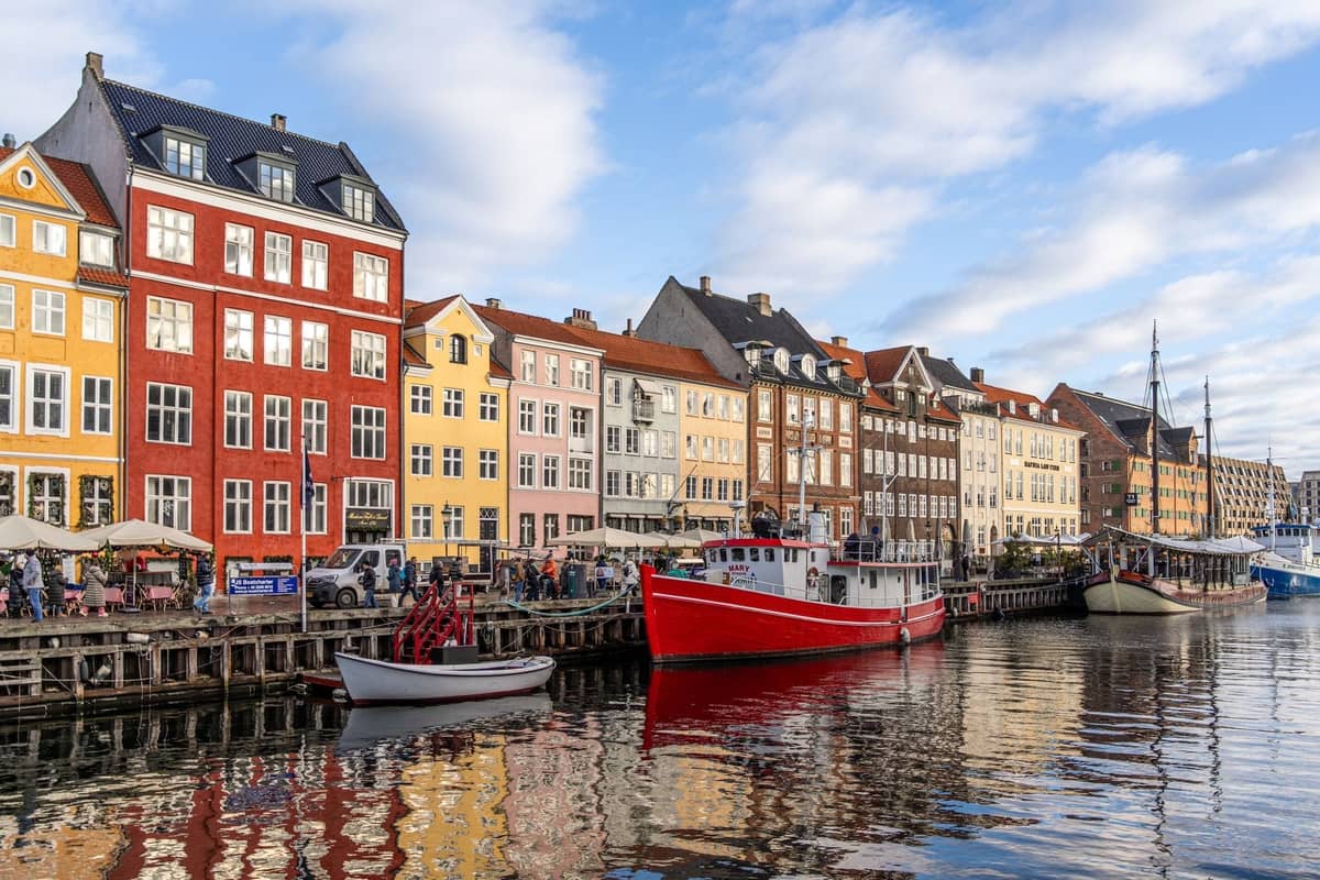 El emblemático paseo marítimo de Nyhavn en Copenhague con coloridos edificios históricos, barcos atracados y personas paseando por el animado muelle.
