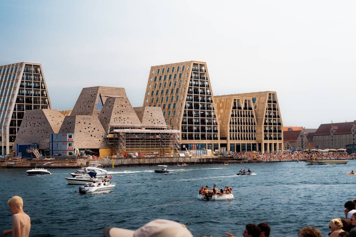 Personas nadando y navegando en el puerto de Copenhague con distintivos edificios modernos al fondo en un día soleado.