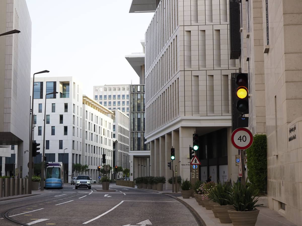 Moderne weiße Gebäude säumen eine saubere, ruhige Straße im Msheireb-Viertel von Doha, mit wenig Verkehr und etwas Begrünung entlang der Gehwege.