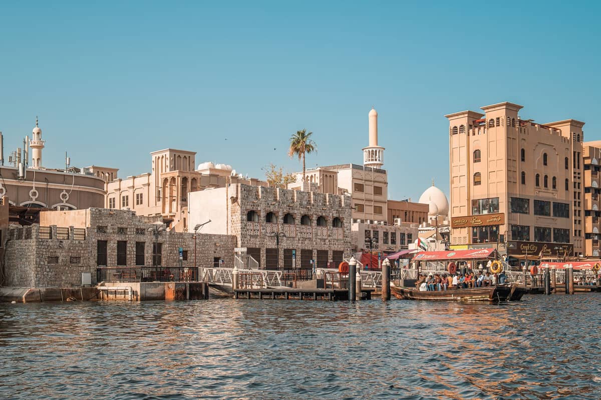 Historische Gebäude und Uferpromenade entlang des Dubai Creek mit Windtürmen, Booten und traditioneller Architektur im Kulturerbe-Viertel von Dubai.