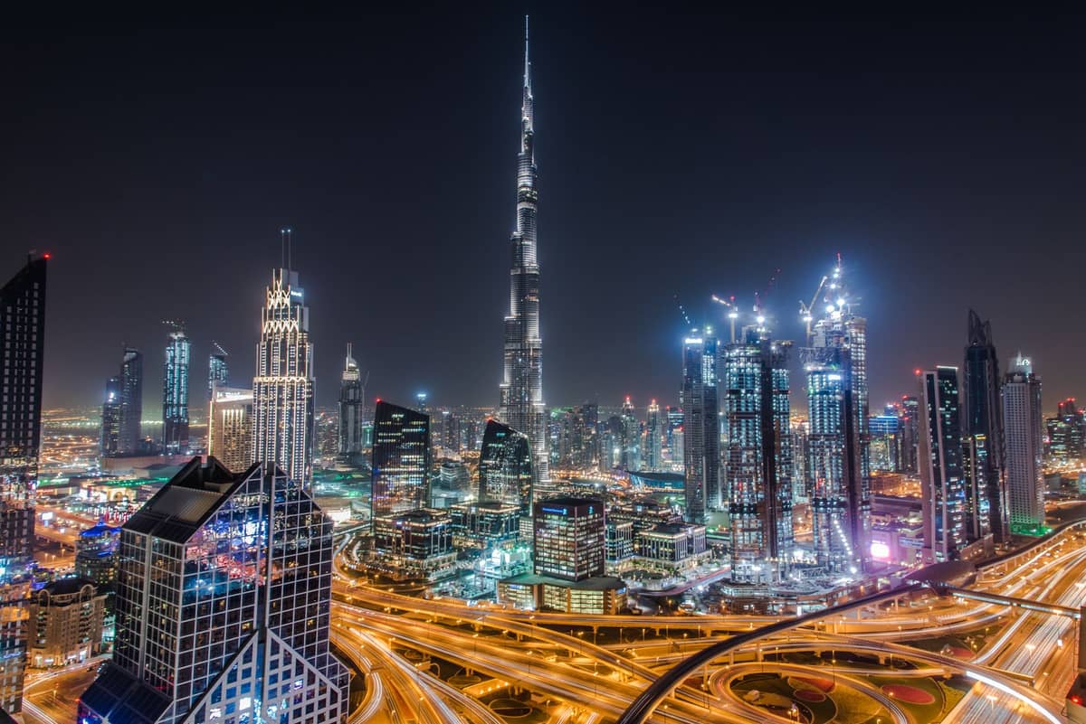 Ein lebhafter Nachtblick auf die Skyline von Dubai mit dem Burj Khalifa und den umliegenden Wolkenkratzern, von oben gesehen mit beleuchteten Highways im Vordergrund.