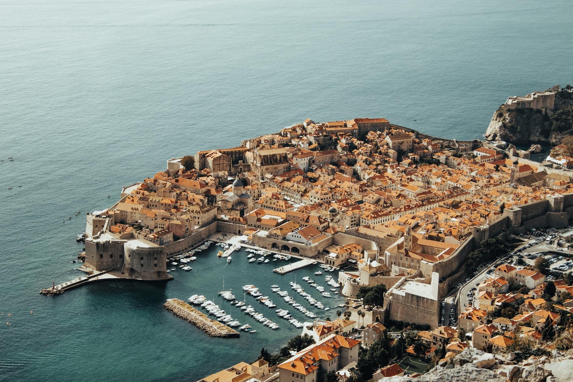 Vue aérienne des remparts fortifiés, du port et des toits orangés de la vieille ville de Dubrovnik, mettant en valeur l'architecture emblématique utilisée comme King's Landing dans Game of Thrones.