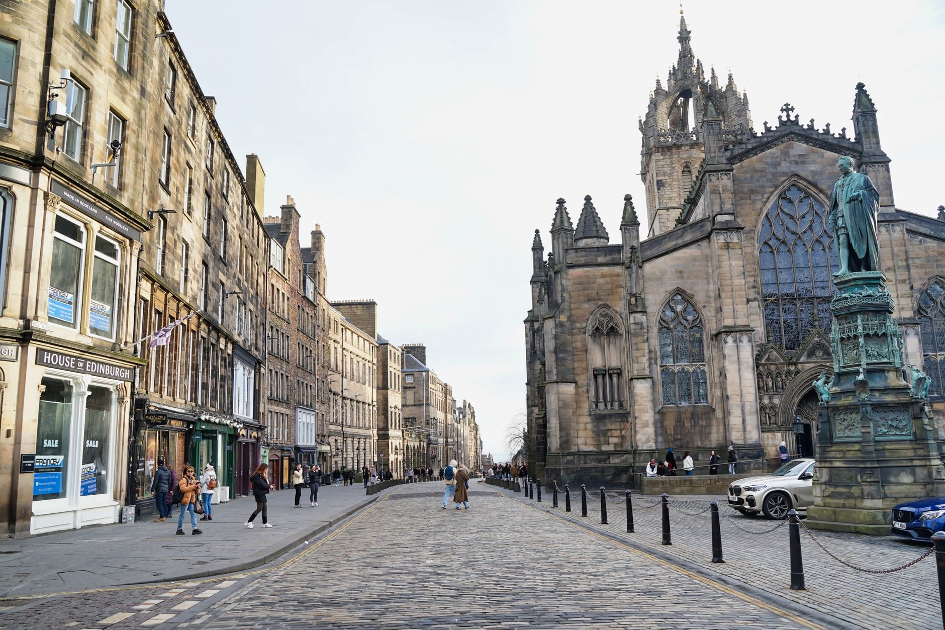 Weitblick auf die Royal Mile in Edinburgh mit der St Giles' Cathedral und historischen Gebäuden entlang der Kopfsteinpflasterstraße, Menschen gehen spazieren und erkunden die Gegend.