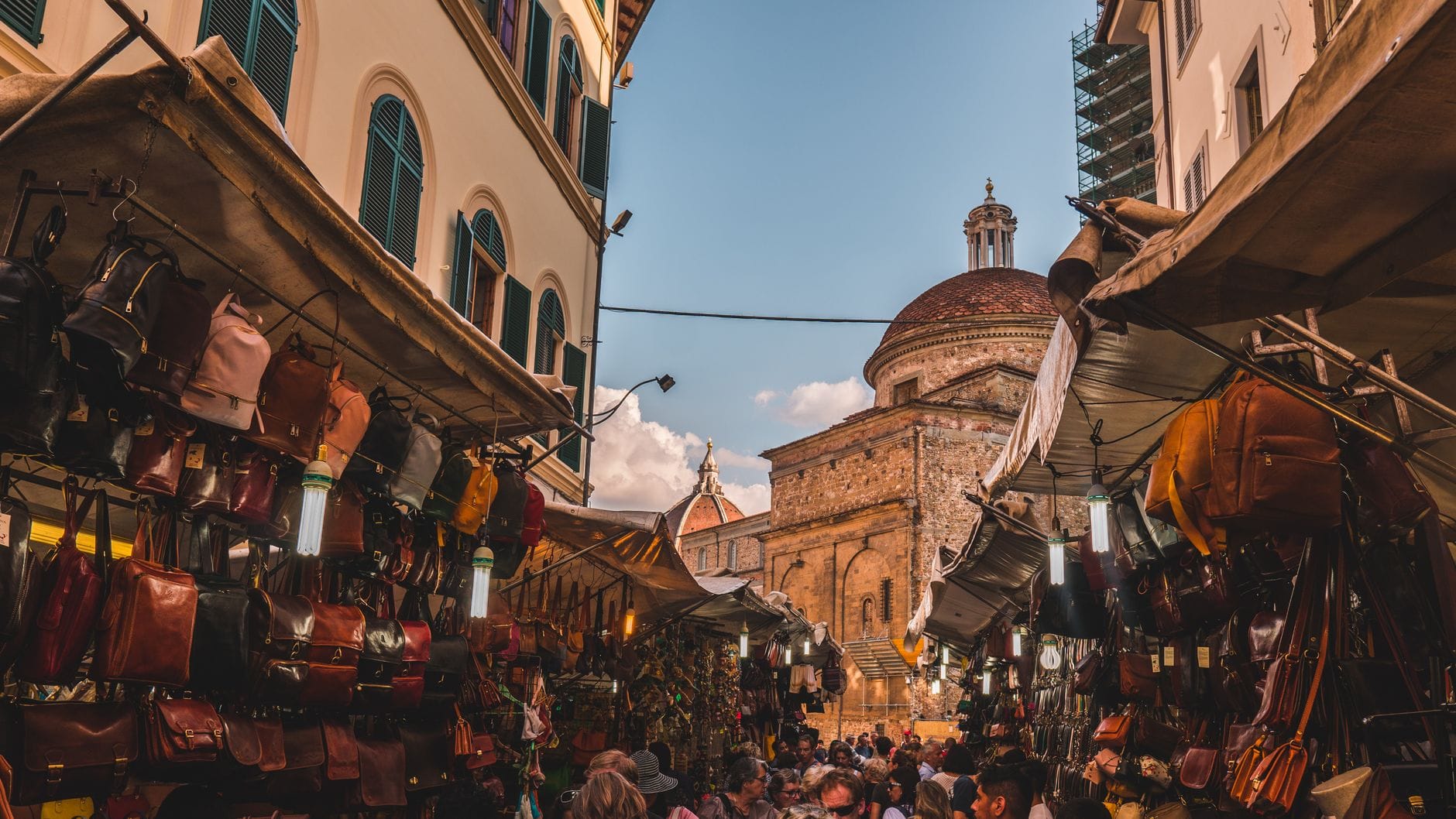 ตลาดหนังกลางแจ้งที่คึกคักในเมือง Florence พร้อมแผงขายของ นักช้อปปิ้ง และโดมอันเป็นเอกลักษณ์ของ Medici Chapel ในพื้นหลัง