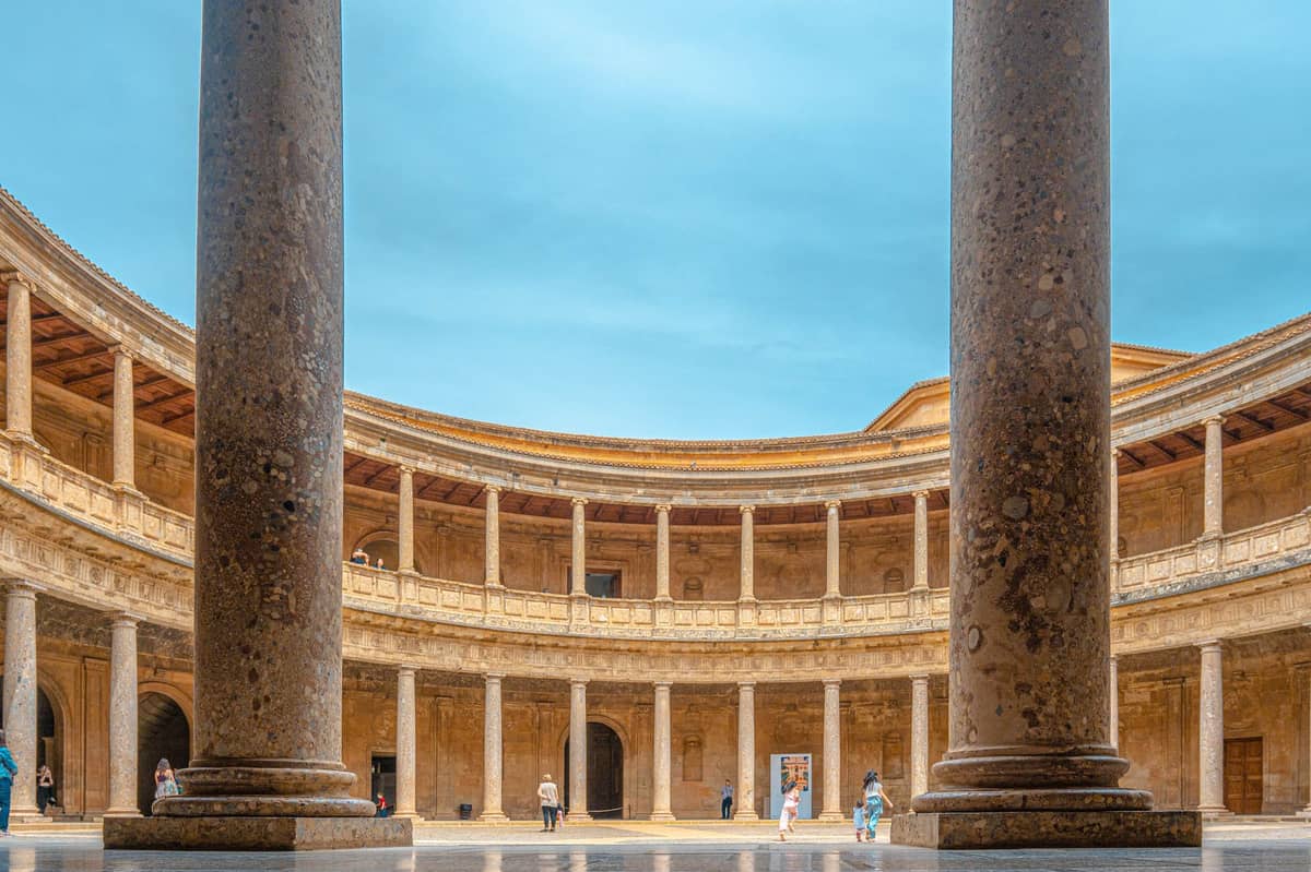 วิวลานภายในสไตล์เรอเนสซองส์ทรงกลมของ Palacio de Carlos V ในเมือง Granada พร้อมผู้คนที่กำลังเดินและท้องฟ้าสีฟ้าด้านบน